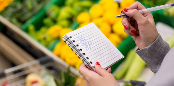 person at a market with a grocery list in one hand and a pen in the other